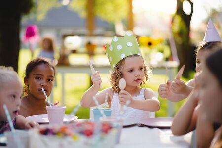 Small children sitting at the table outdoors on garden party, eating.の写真素材