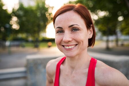 Front view of young woman standing outdoors in city, resting after exercise.