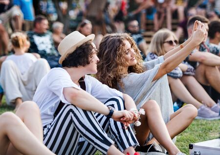 Group of young friends sitting on ground at summer festival.
