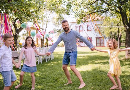 Man with kids on birthday party playing outdoors in garden in summer.