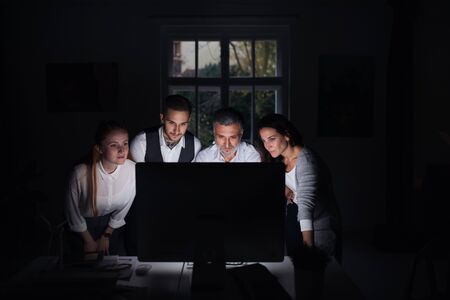 Group of businesspeople with computer indoors in office, working late.