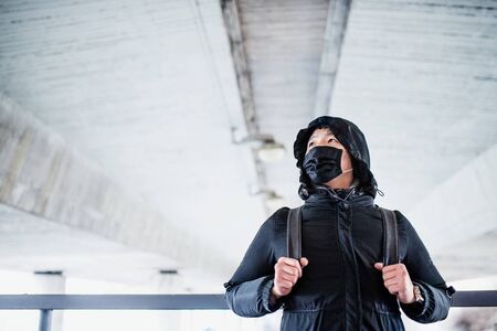Man in black clothes and respirator standing outdoors in city, coronavirus concept.