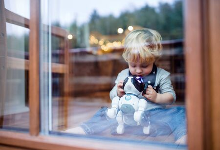 A cute toddler boy sitting indoors at home, playing with robotic dog.の写真素材