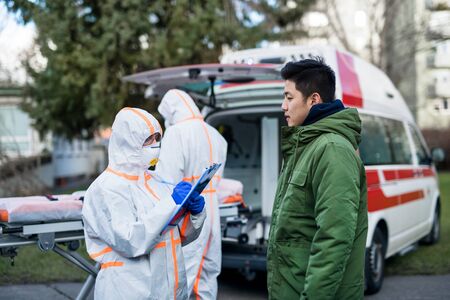 People with protective suits helping man outdoors, coronavirus concept.の写真素材