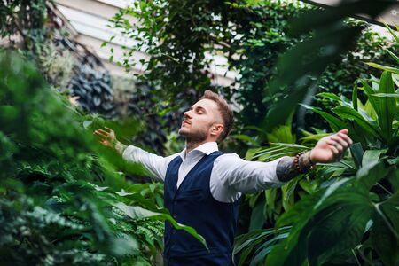 Young man standing in botanical garden, arms stretched.の写真素材