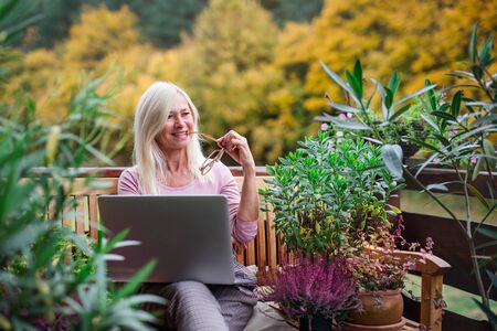 Senior woman with laptop sitting outdoors on terrace, working.の写真素材