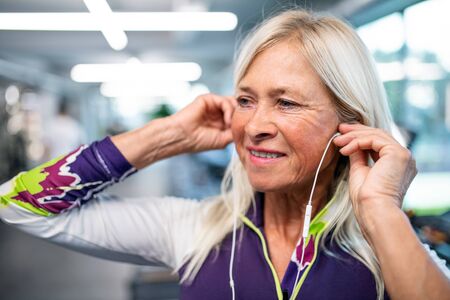 A senior woman with earphones in gym resting after doing exercise.