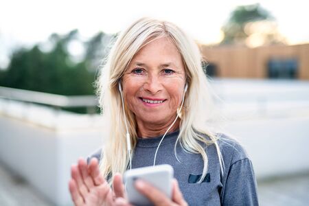 A senior woman with smartphone outdoors resting after exercise.の写真素材