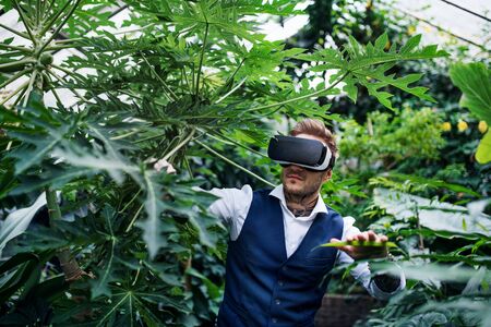 Front view of young man standing in botanical garden, using VR glasses.の写真素材