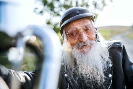 A senior man traveller with motorbike in countryside.