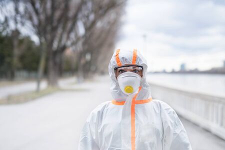 Woman with protective suit and respirator standing outdoors, coronavirus concept.