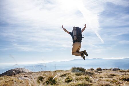 Rear view of mature man with backpack hiking in mountains in summer, jumping.の写真素材