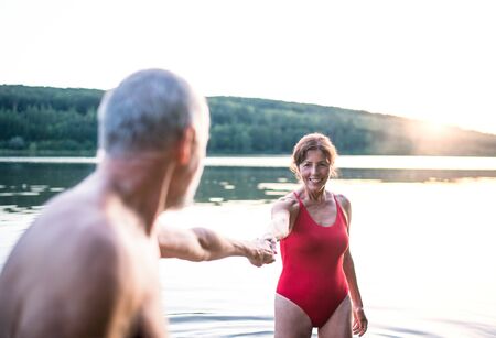 Senior couple in swimsuit standing in lake outdoors before swimming.の写真素材