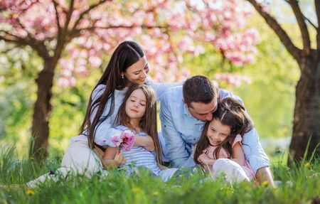 Young parents with small daugthers sitting outside in spring nature.の写真素材