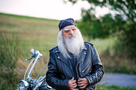 Senior man traveller with motorbike and sunglasses in countryside.