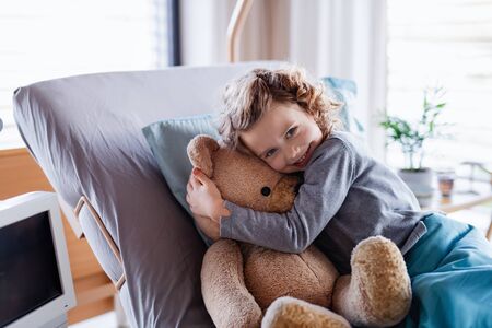 Smiling small girl with teddy bear in bed in hospital.の写真素材