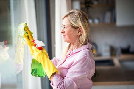 Portrait of senior woman cleaning windows indoors at home.の写真素材