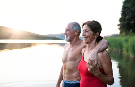 Senior couple in swimsuit standing by lake outdoors before swimming.の写真素材