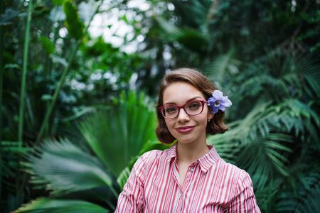 Young woman standing in botanical garden, looking at camera.