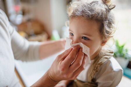 Unrecognizable father blowing nose of small sick daughter indoors at home.の写真素材