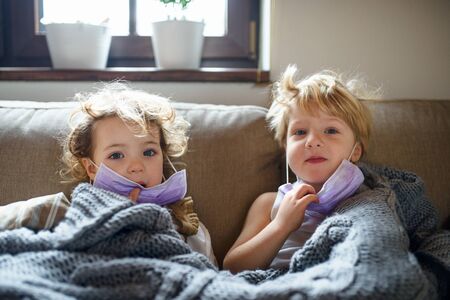 Two small sick children with face mask at home lying in bed.