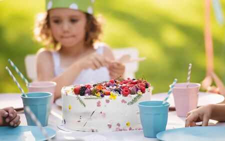Small girl with cake celebrating birthday outdoors in garden in summer, party concept.の写真素材