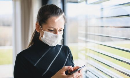 Worried woman with telephone and face masks indoors at home, Corona virus concept.