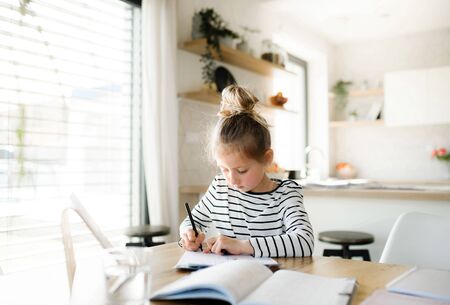 Small girl learning indoors at home, Corona virus and quarantine concept.