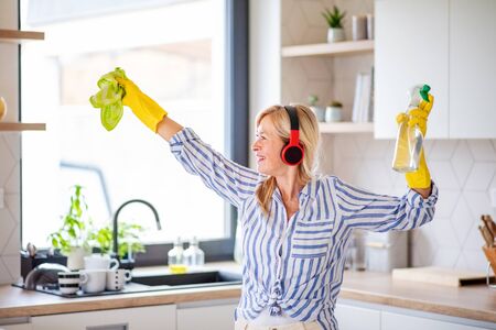 Portrait of senior woman with headphones and gloves cleaning indoors at home.の写真素材