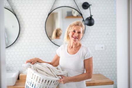 Portrait of senior woman with laundry basket indoors at home.の写真素材