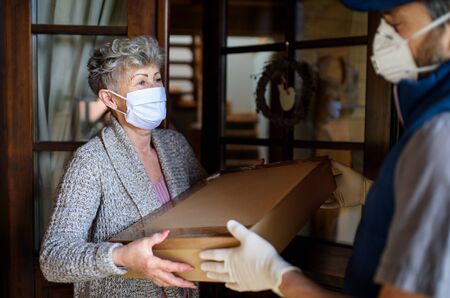 Courier with face mask delivering parcel to senior woman, corona virus and quarantine concept.の写真素材