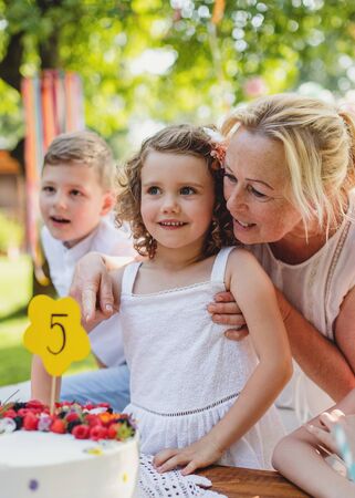 Small girl with cake celebrating birthday outdoors in garden in summer, party concept.の写真素材