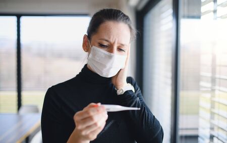 Worried woman with thermometer and face masks indoors at home, Corona virus concept.の写真素材