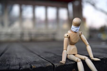 Sad wooden mannequin with face mask in town, corona virus and lockdown concept.の写真素材