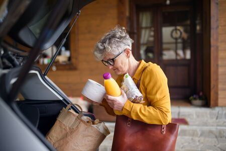 Senior woman with shopping in bag standing outdoors by car.の写真素材