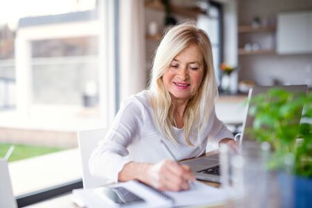 Senior woman with laptop indoors in home office, working.の写真素材