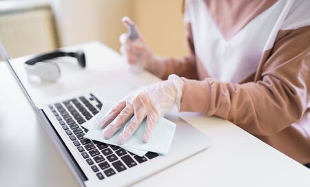Unrecognizable young student with gloves at the table, disinfecting laptop.の写真素材