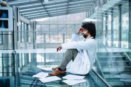 Worried and tired doctor sitting on floor in hospital, corona virus concept.