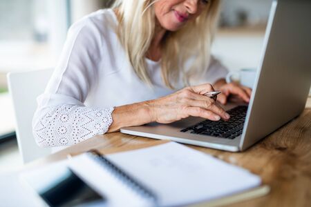 Unrecognizable senior woman with laptop indoors in home office, working.の写真素材