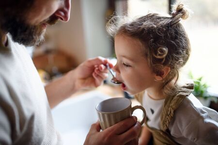 Unrecognizable father giving syrup to small sick daughter indoors at home.の写真素材