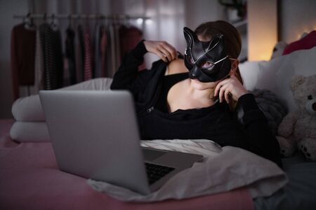Young girl with cat mask and laptop indoors online dating and abuse concept.の写真素材