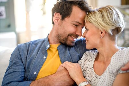 Happy couple in love sitting indoors at home, hugging.