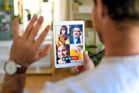 Rear view of unrecognizable man having video call on tablet at home.