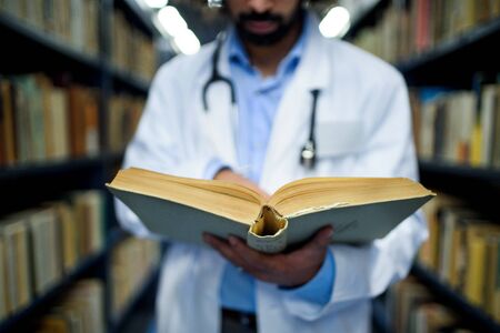 Unrecognizable doctor in library, studying information about corona virus.の写真素材