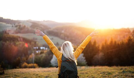 Rear view of senior woman hiker standing outdoors in nature at sunset.