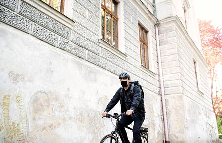 Delivery man courier with face mask and bicycle cycling in town.