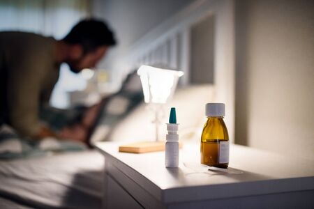 Bottle of syrup medication on bedsite table at home, medicine and sickness concept.