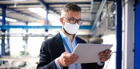 Technician or engineer with protective mask and tablet working in industrial factory.の写真素材