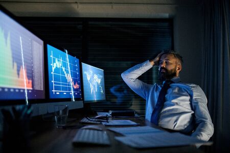 Frustrated businessman with computer sitting at desk, working late. Financial crisis concept.の写真素材