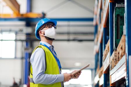 Technician or engineer with protective mask and helmet working in industrial factory.